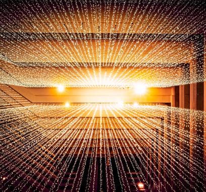 Abstract view looking up at an atrium with strings of golden lights radiating from a central point, symbolizing the broad network reach and connectivity of messaging services.